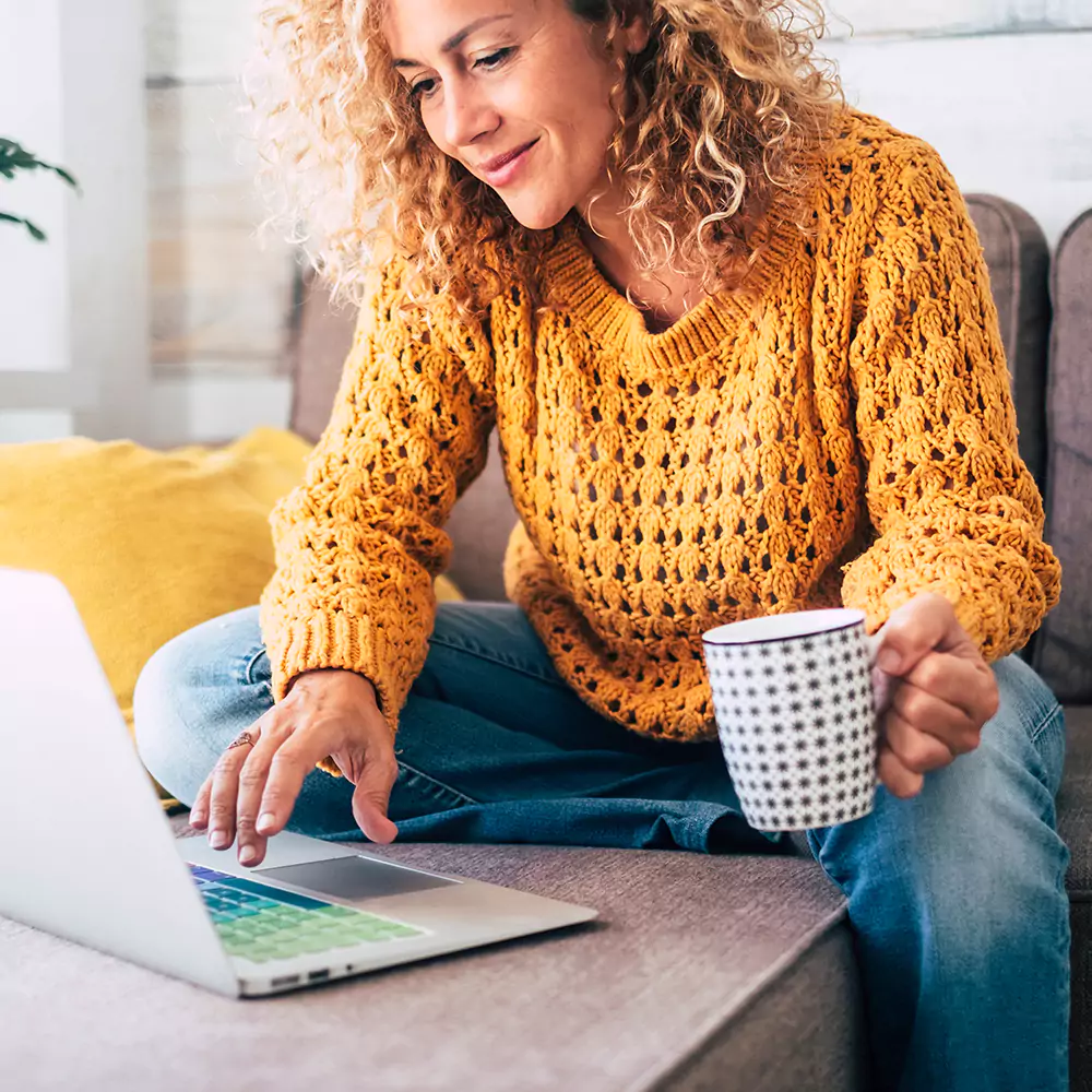 A woman in a yellow jumper working on her computer