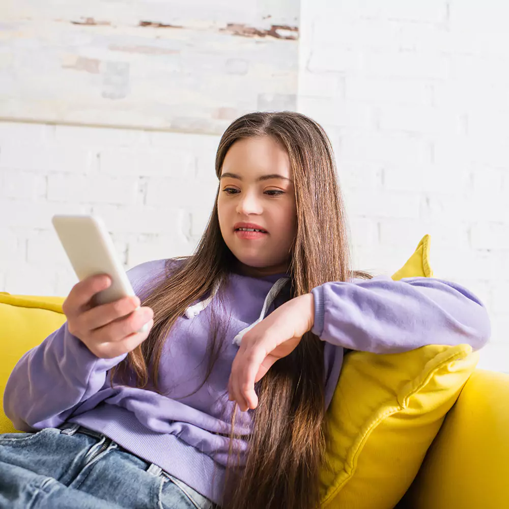 A down syndrome woman using her phone indoors on the couch