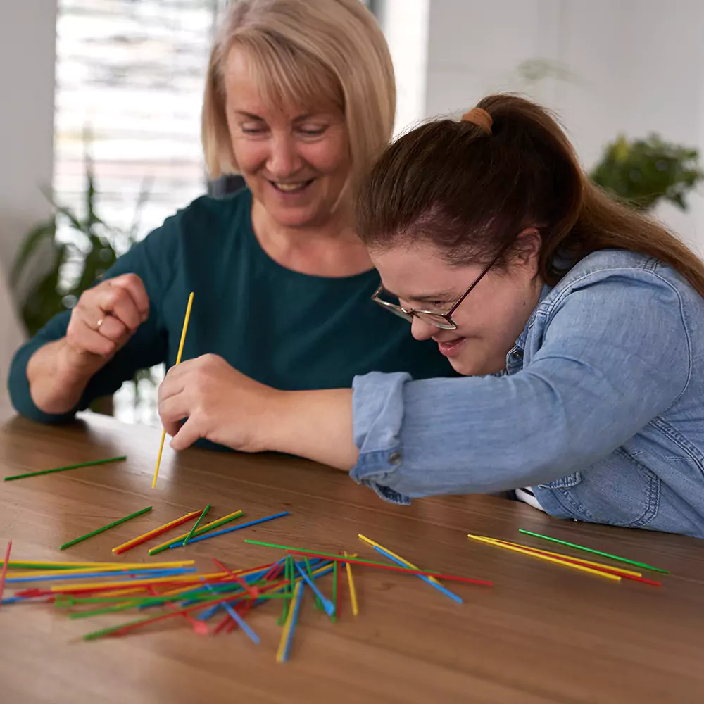A care giver and a down syndrome woman playing pick up sticks