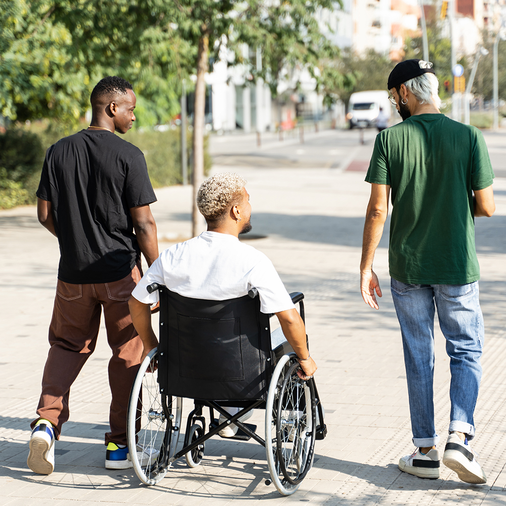 3 friends, one in a wheelchair walking outdoors in the park